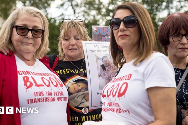 Four women who have been affected by the infected blood scandal attend a vigil in Parliament Square on 19 May, 2024 in London, England. Two of the women wear white t-shirts with "contaminated blood" printed on them in red ink.